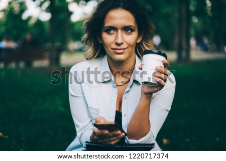 Attractive female blogger spending free time at summer street and shopping online using application on telephone.Young charming woman enjoying recreation sitting in garden while checking notification