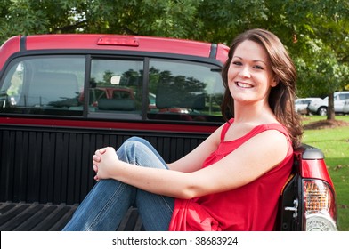 Attractive Female Brunette Sitting In Bed Of Red Pickup Truck.