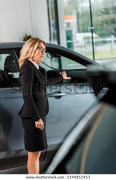 attractive\
female car dealer pointing at car in\
showroom