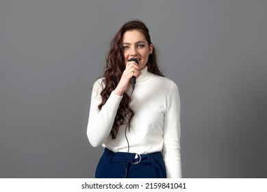 Attractive Female Conference Speaker During Presentation, Holds Microphone And Makes Some Gestures, Isolated On Gray