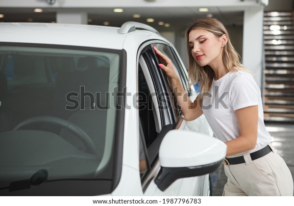 Attractive female customer looking\
inside new automobile for sale at car dealership, copy\
space