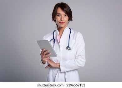 Attractive female doctor holding digital tablet in her hand while standing at isolated grey background. Copy space. - Powered by Shutterstock