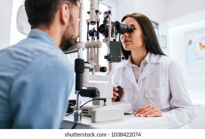 Attractive Female Doctor  Ophthalmologist Is Checking The Eye Vision Of Handsome Young Man In Modern Clinic. Doctor And Patient In Ophthalmology Clinic.