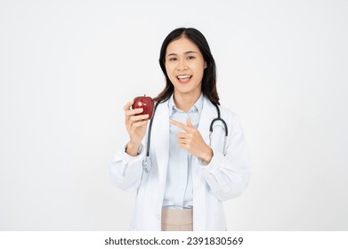 Attractive female doctor with a white coat smiling and holding an apple. Cheerful medical nutritionist recommending a healthy diet to a patient.