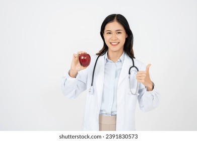 Attractive female doctor with a white coat smiling and holding an apple. Cheerful medical nutritionist recommending a healthy diet to a patient.