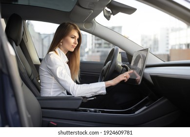 Attractive Female Driver In Formal Wear, Operating The Touchscreen On The Dashboard In Her Electric Car Inputting Data Before Commencing To Drive. View From Inside The Vehicle