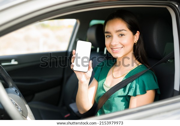 Attractive female driver\
showing her smartphone screen and ready to pick up a passenger on a\
ride share app