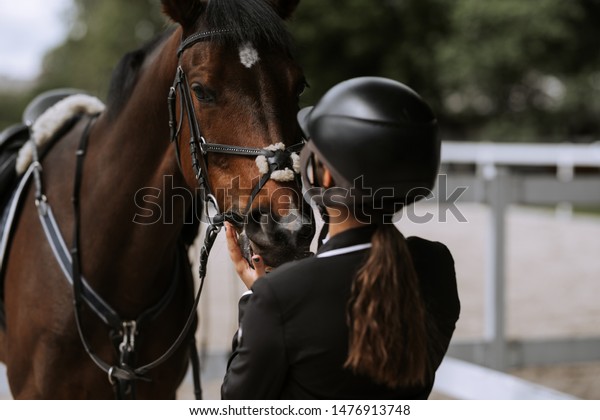 Attractive female equestrian in riding helmet
looking at horse in horse
club.