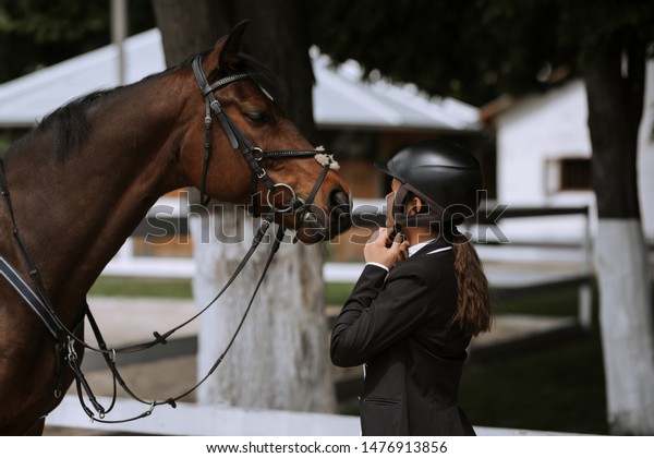 Attractive female equestrian in riding helmet\
looking at horse in horse\
club.