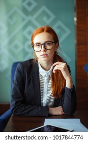 Attractive female financier wearing glasses work on digital tablet during break, young serious businesswoman using touch pad and looking at camera