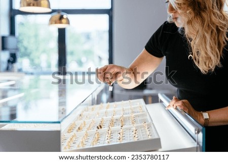 Attractive female jewelry seller standing behind counter put gold ring on a display at modern jewelry shop. Luxury jewelry store concept. Luxury jewelry store concept.