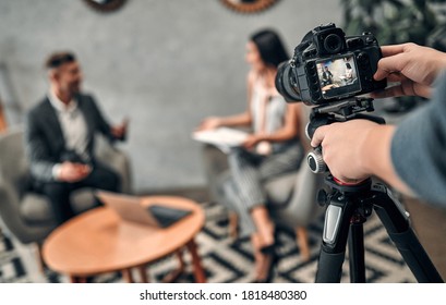 Attractive female journalist interviewing handsome business man with cameraman on the foreground