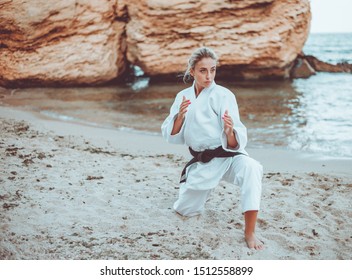 Attractive female martial artist in a white kimono with a black belt stands in fighting stance on wild beach - Powered by Shutterstock