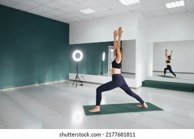 Attractive Female Middle Age 50 Years Old Doing Standing Hero Yoga Pose Near Big Mirror In Empty Yoga Studio