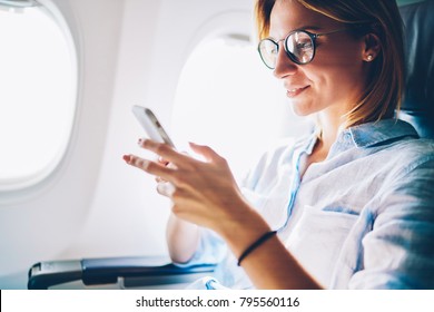 Attractive female passenger of airplane read news from networks via smartphone and wifi on board, young woman sending message on phone traveling by plane in first class connecting to wireless on phone