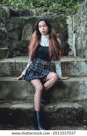 An attractive female student in a fashionable gothic outfit. Sitting on a flight of concrete steps outdoors.