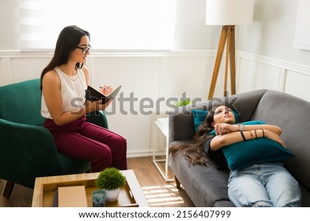 Attractive female therapist with glasses asking questions about her problems to a sad teen girl during a therapy session