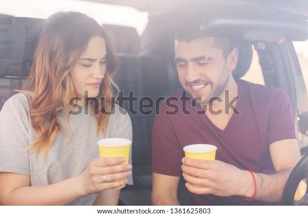 Attractive female and unshaven male couple have\
coffee break in auto, reach destination wih high speed. Happy\
family spend time together, travel on weekend, enjoying cool\
vocation. Travelling\
concept.