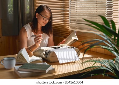 Attractive female writer in glasses looking for inspiration to start a new novel on her retro writing machine. Journalist woman sitting at desktop creating job article at her home office. Distance job