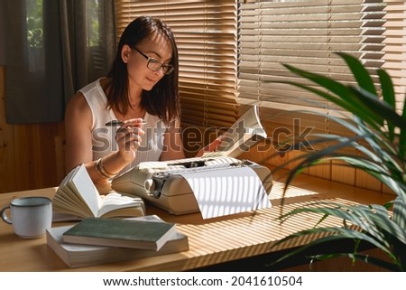 Attractive female writer in glasses looking for inspiration to start a new novel on her retro writing machine. Journalist woman sitting at desktop creating job article at her home office. Distance job 商業照片 © 