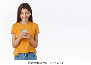 Attractive Feminine Young Woman With Long Hair Wear Wireless Earphone, Smiling And Laughing Watching Video In Crowded Cafe, Look Smartphone Happy, Listen Music Or Pick Song In Playlist