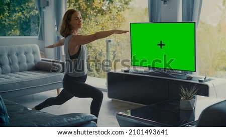 Attractive fit girl doing yoga in living room with Green Screen TV