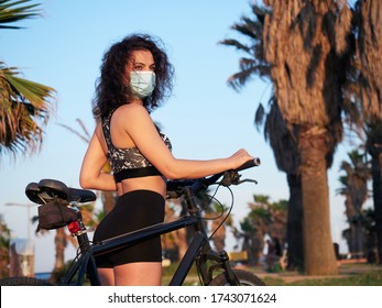 Attractive and fit girl in sportswear, riding her bike in a park with a protection mask to avoid contagion of Covid-19. New normal. - Powered by Shutterstock