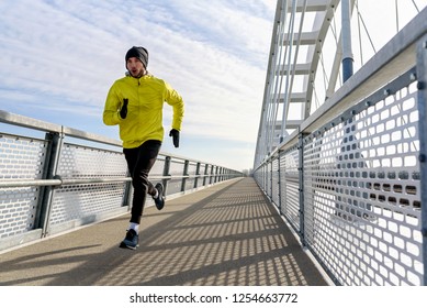 Attractive Fit Man Running Fast Along Big Modern Bridge. Exercising, Jogging, Sport, Winter. Male Athlete Running.