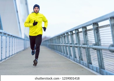 Attractive Fit Man Running Fast Along Big Modern Bridge. Exercising, Jogging, Sport, Winter. Male Athlete Running.