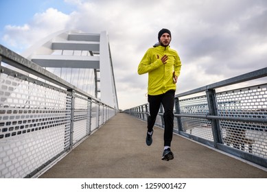 Attractive Fit Man Running Fast Along Big Modern Bridge. Exercising, Jogging, Sport, Winter. Male Athlete Running.