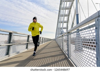 Attractive Fit Man Running Fast Along Big Modern Bridge. Exercising, Jogging, Sport, Winter. Male Athlete Running.