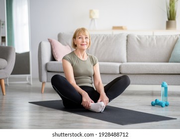 Attractive fit mature lady sitting in butterfly yoga pose on sports mat at home, copy space. Motivated senior woman doing flexibility exercises, keeping fit and healthy. Active lifestyle concept