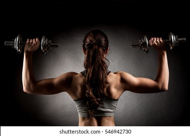 Attractive fit woman works out with dumbbells as a fitness conceptual over dark background.