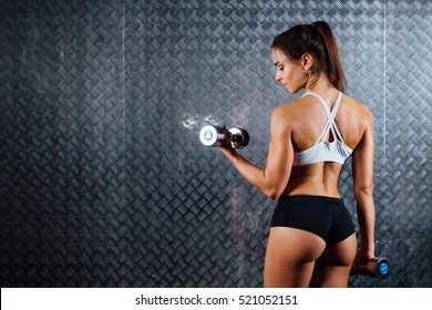 Attractive fitness woman with dumbbell indoor portrait, trained female body, studio caucasian model. Grey metal surface with a bumpy pattern background. - Powered by Shutterstock