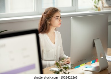 Attractive Focused Female Employee Intern Working On Desktop Sitting At Coworking Space Shared Office Desk, Serious Young Pretty Businesswoman Worker Using Pc Computer At Workplace Looking At Monitor