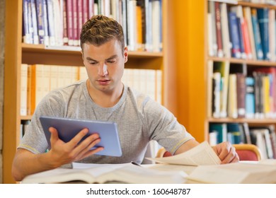 Attractive focused student using tablet and turning page in library