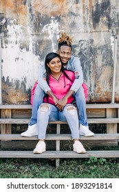 An Attractive And Fun African-American Couple Sitting Outside On Steps In An Urban Setting With A Jacket And Denim Jeans