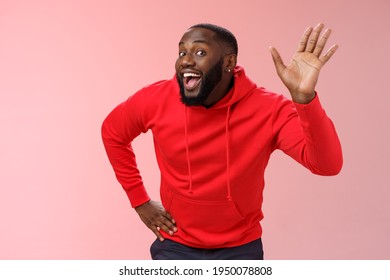 Attractive funny african american gay beard in red hoodie raise palm waving hello hi howdy gesture acting feminine cute fool around welcoming guests greeting standing pink background