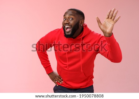 Attractive funny african american gay beard in red hoodie raise palm waving hello hi howdy gesture acting feminine cute fool around welcoming guests greeting standing pink background