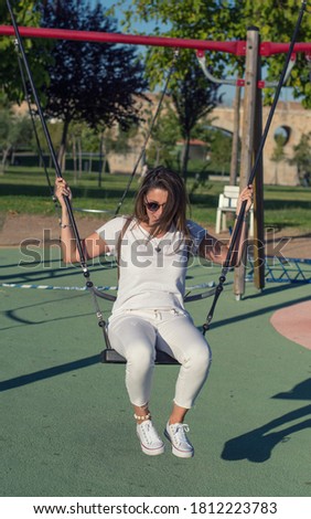 Attractive and funny woman, swinging on the swings in a park.
Woman who remembers her childhood in a park.