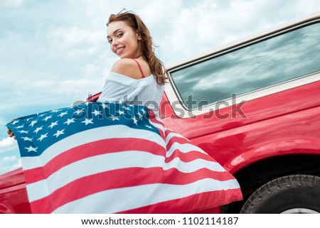 attractive girl with american flag standing near red car