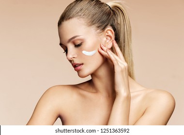 Attractive girl applying moisturizing cream on her face. Photo of young girl with flawless skin on breige background. Skin care and beauty concept