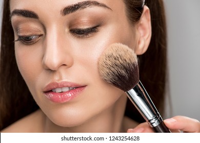 attractive girl applying powder on face with cosmetic brush