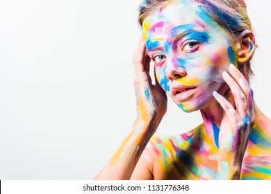 attractive girl with colorful bright body art touching face and looking at camera isolated on white 