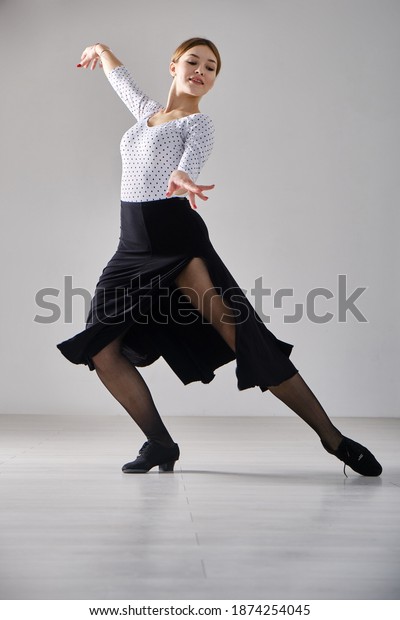 Attractive girl dances ballroom dancing in front of\
a mirror in a bright white hall. A professional ballroom dancer\
trains in a choreographic\
hall.