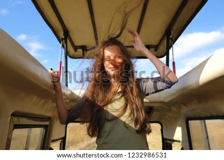 Attractive girl grimaces and laughs Young woman with wind in her long hair in the car on a safari Blue sky