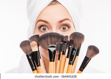 Attractive girl hiding behind makeup brushes