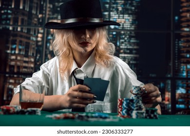 attractive girl holding cards and poker chips at casino table hiding her gaze. player girl poker. casino - Shutterstock ID 2306333277