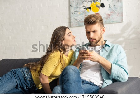 Attractive girl looking at dependent boyfriend with smartphone on couch