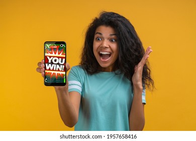 Attractive Girl With Perfect Smile Showing Sincere Excitement About Victory At Bookmaker's Website. Girl Being Happy Winning Bet In Online Sport Gambling Application On Her Mobile Phone.